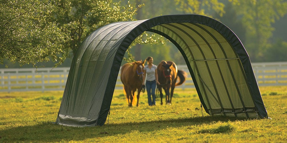 a woman leading two horses into a run-in shelter